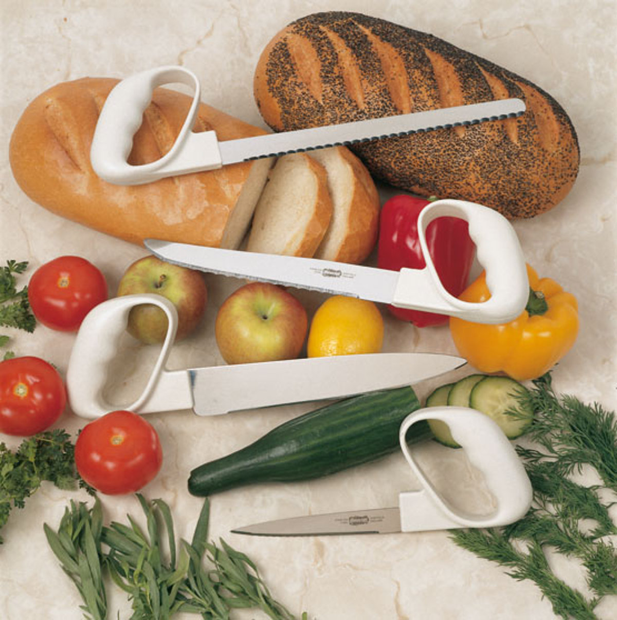 Bild zeigt zwei Brote, Paprika, Tomaten und Gurken. Darauf liegen vier Messer mit Griffverstärkung und unterschiedlichen Klingen.