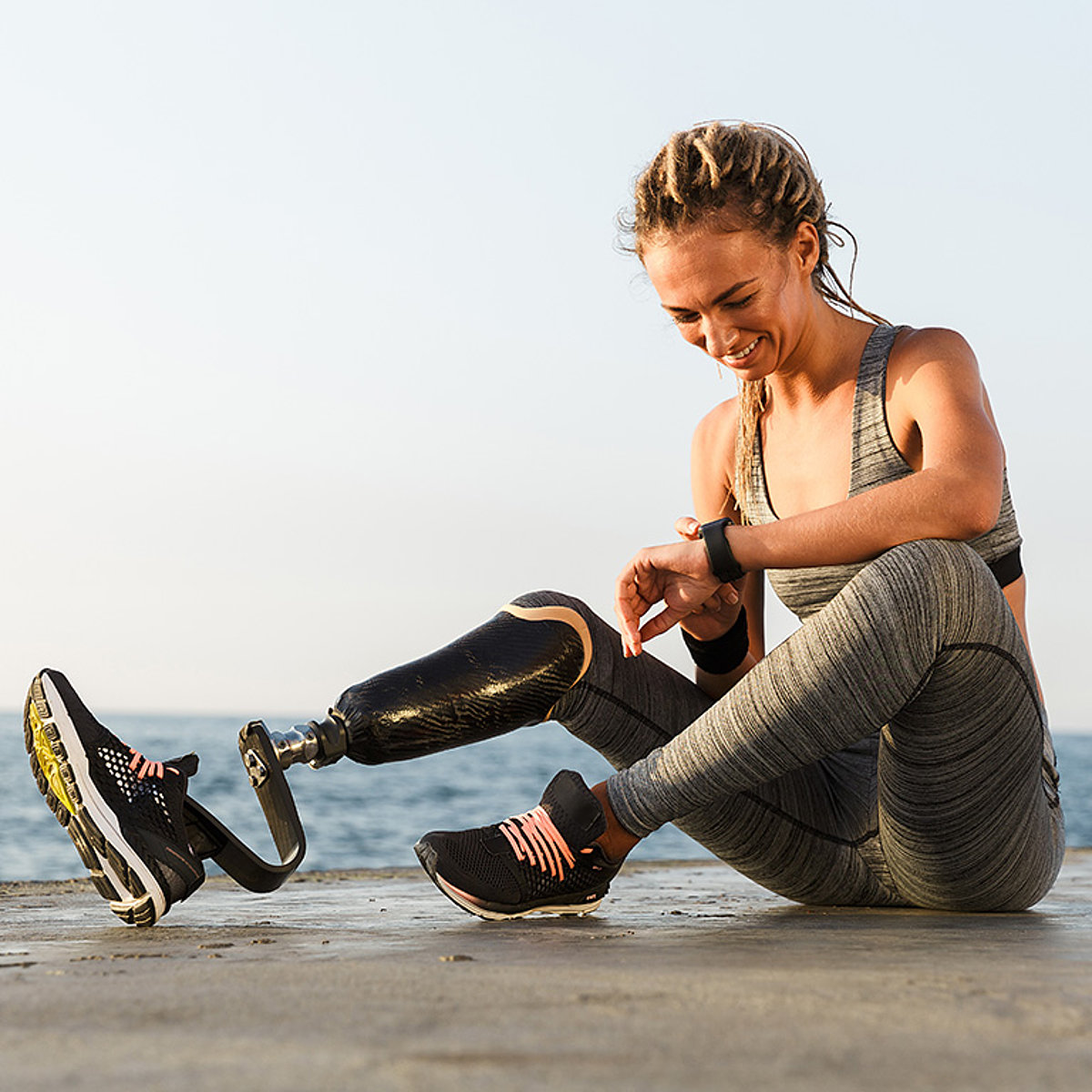 Eine junge Joggerin mit Beinprothese ruht sich am Strand aus.